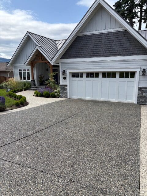 A clean, professionally sealed exposed aggregate driveway with a "wet-look" finish in front of a modern home in Victoria, BC