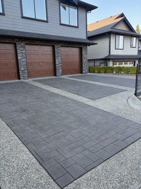 A freshly sealed driveway featuring dark grey stamped concrete pavers with an exposed aggregate border in Victoria, BC