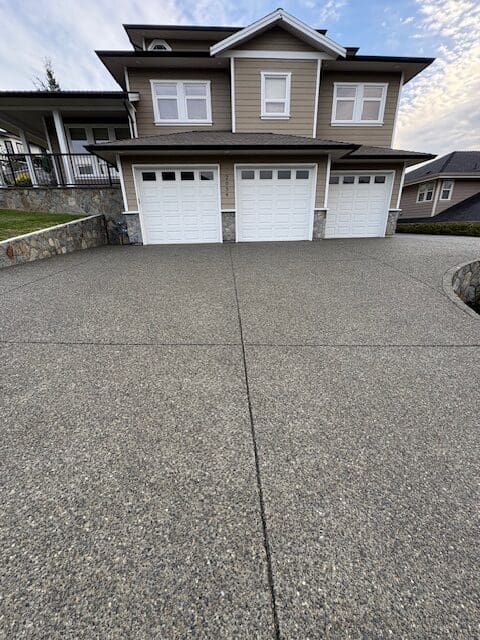 A clean, well-maintained exposed aggregate concrete driveway and retaining wall in front of a modern home, showing the benefits of professional concrete sealing in Victoria, BC